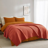 Bed with orange bedding and a red throw blanket in a bedroom setting.