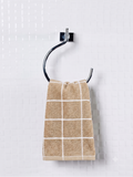 A beige hand towel with a white grid pattern hangs from a black metal hook on a white tiled wall.