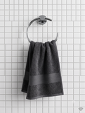 A dark charcoal gray towel with a matching horizontal stripe hangs from a silver metal ring on a white tiled wall.