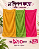 Three colorful pith towe towels in yellow, green, and pink are displayed side-by-side against a warm beige background with decorative plants and Bengali promotional text.