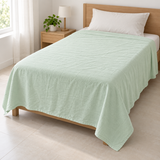 A light mint green textured cotton sheet or duvet cover spread across a wooden bed frame in a bright, modern bedroom setting.