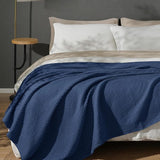Blue textured blanket on a bed with white pillows and a dark gray wall.
