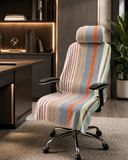 A high-back office chair with a striped fabric slipcover draped over it, set in a modern home office environment next to a desk and a potted plant.