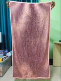 A pink and black vertically striped bath towel held up by two hands in an indoor setting with a green wall and blue curtain in the background.