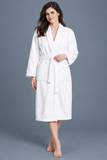 A woman modeling a white bathrobe with a tie belt and front patch pockets, standing against a plain gray studio background.